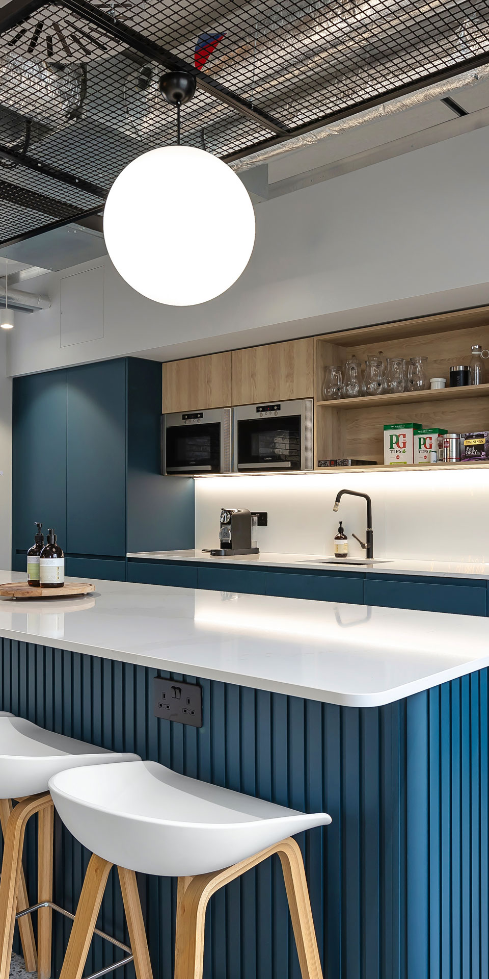 Office kitchen with blue cabinets, tea points, marble breakfast bar and white stools