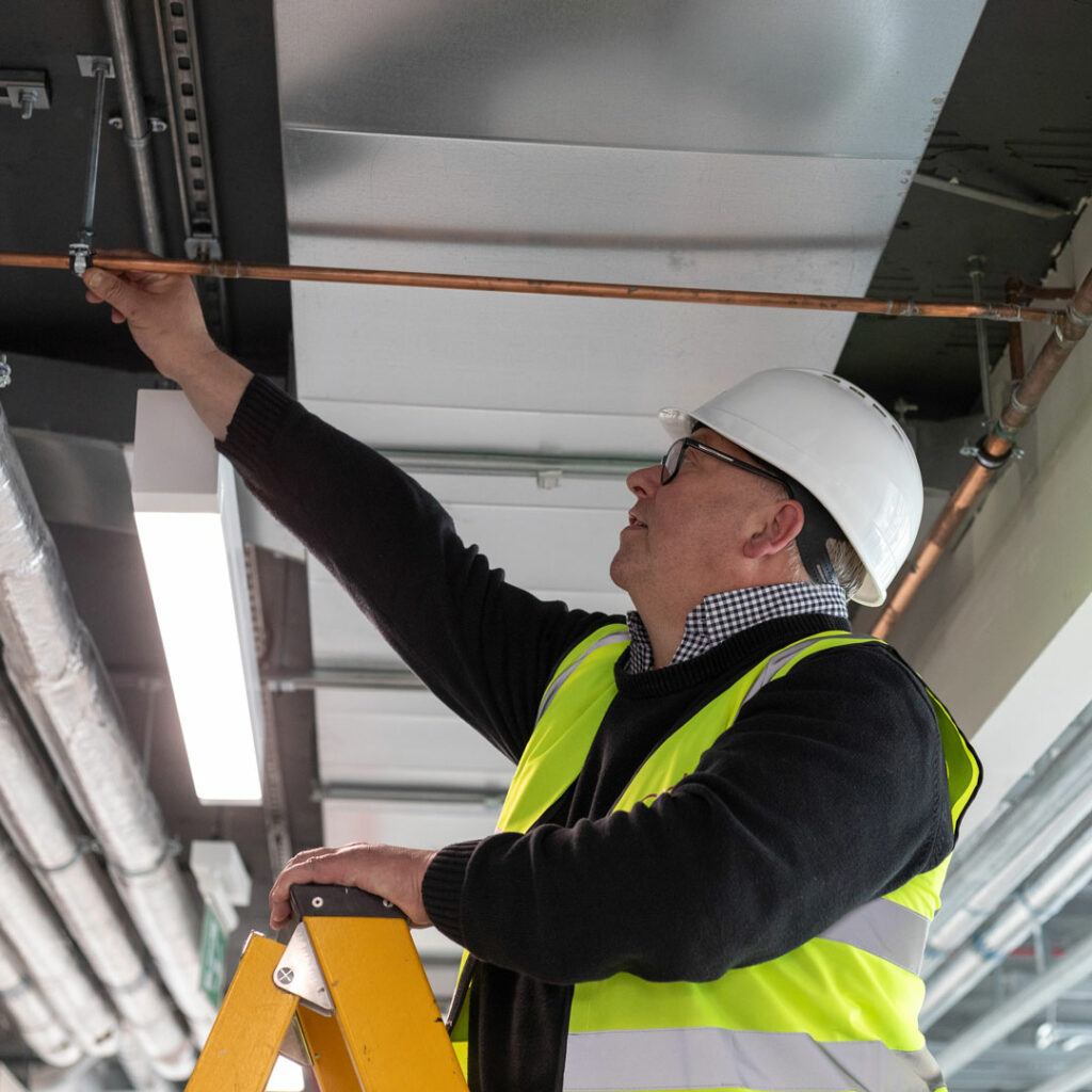 A building specialist inspecting pipe work on a ladder