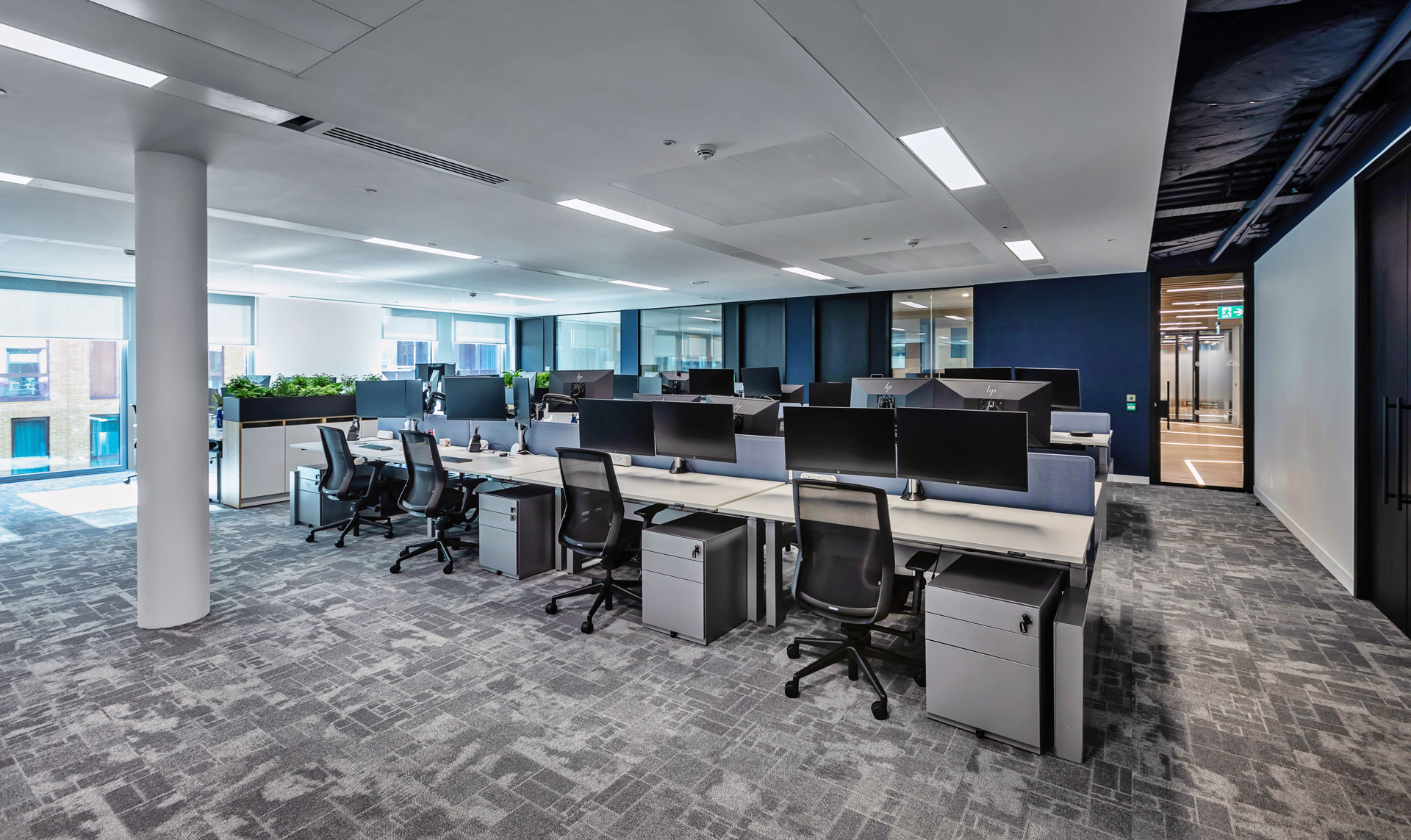 Open plan office with blue walls and desks in a row with filing cabinets and computer monitors